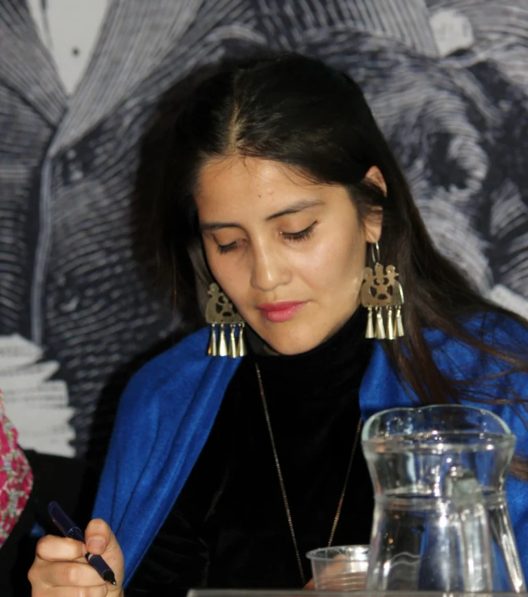 Mujer de cabello oscuro escribiendo junto a una jarra de agua.